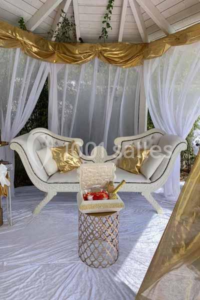 Deux canapés blancs ornés de coussins dorés sous une tonnelle décorée de rideaux blancs et de drapés dorés.