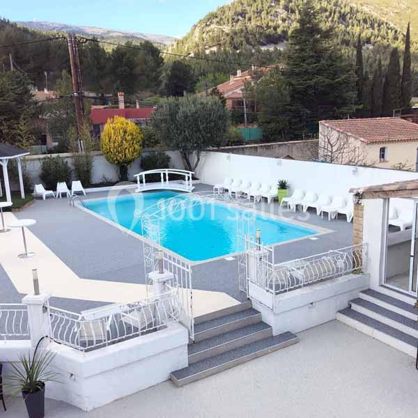 Piscine extérieure entourée de chaises blanches, située dans une cour avec vue sur des collines et des arbres.