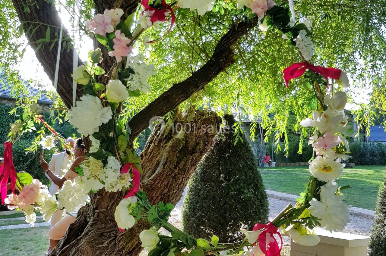 Couronne de fleurs blanches et roses suspendue à un arbre sous la lumière du soleil dans un jardin verdoyant.