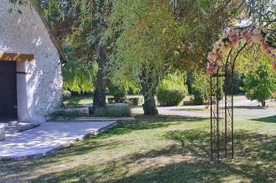 Miniature Location salle Longnes (Yvelines) - Domaine des Clos Vallées #11 Couronne de fleurs blanches et roses suspendue à un arbre sous la lumière du soleil dans un jardin verdoyant.