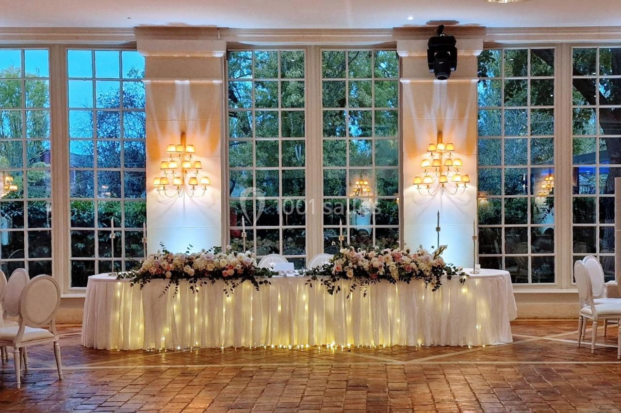 Salle de réception élégante avec grandes baies vitrées, tables décorées de fleurs et éclairage chaleureux.