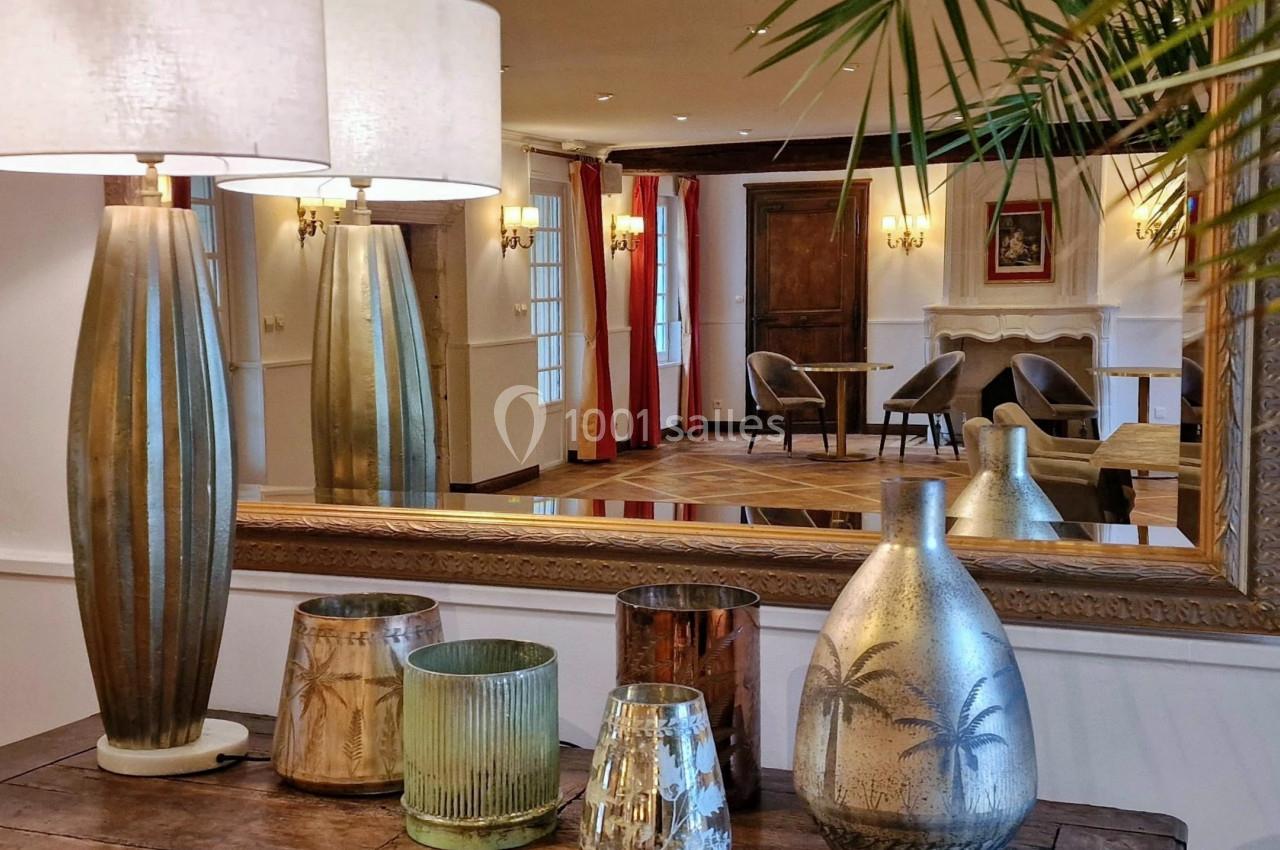 Lampes et vases décoratifs sur une table en bois, reflétés dans un grand miroir d'une pièce élégante et lumineuse.