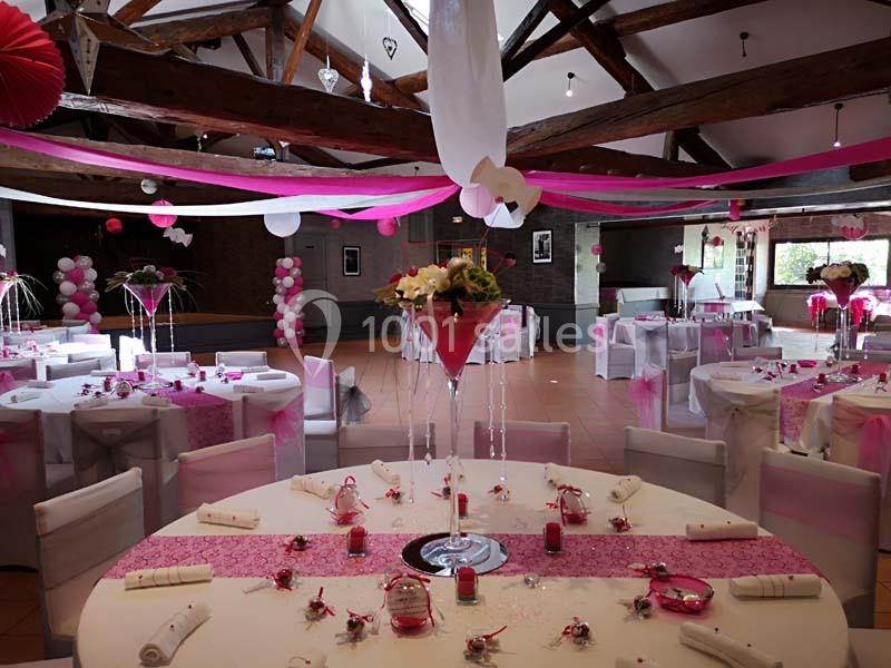 Salle de réception décorée pour un mariage avec des tables dressées, des nappes blanches et des ornements roses.