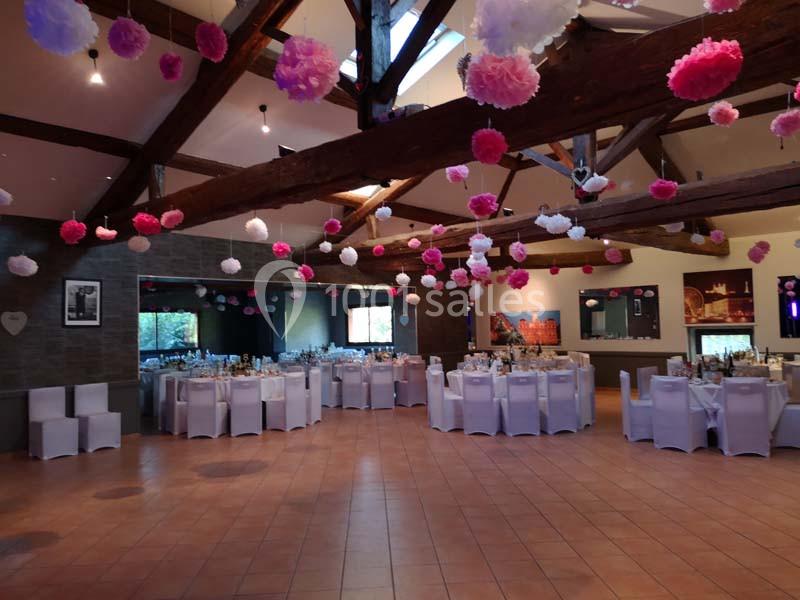 Salle de réception décorée avec des tables dressées, des chaises blanches et des suspensions en papier rose et blanc.