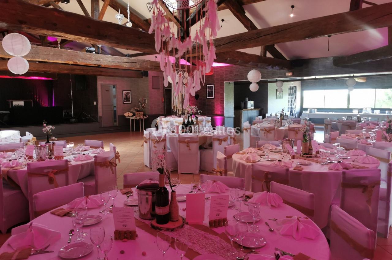 Salle de réception décorée pour un événement, avec tables rondes dressées, nappes blanches et éclairage tamisé.