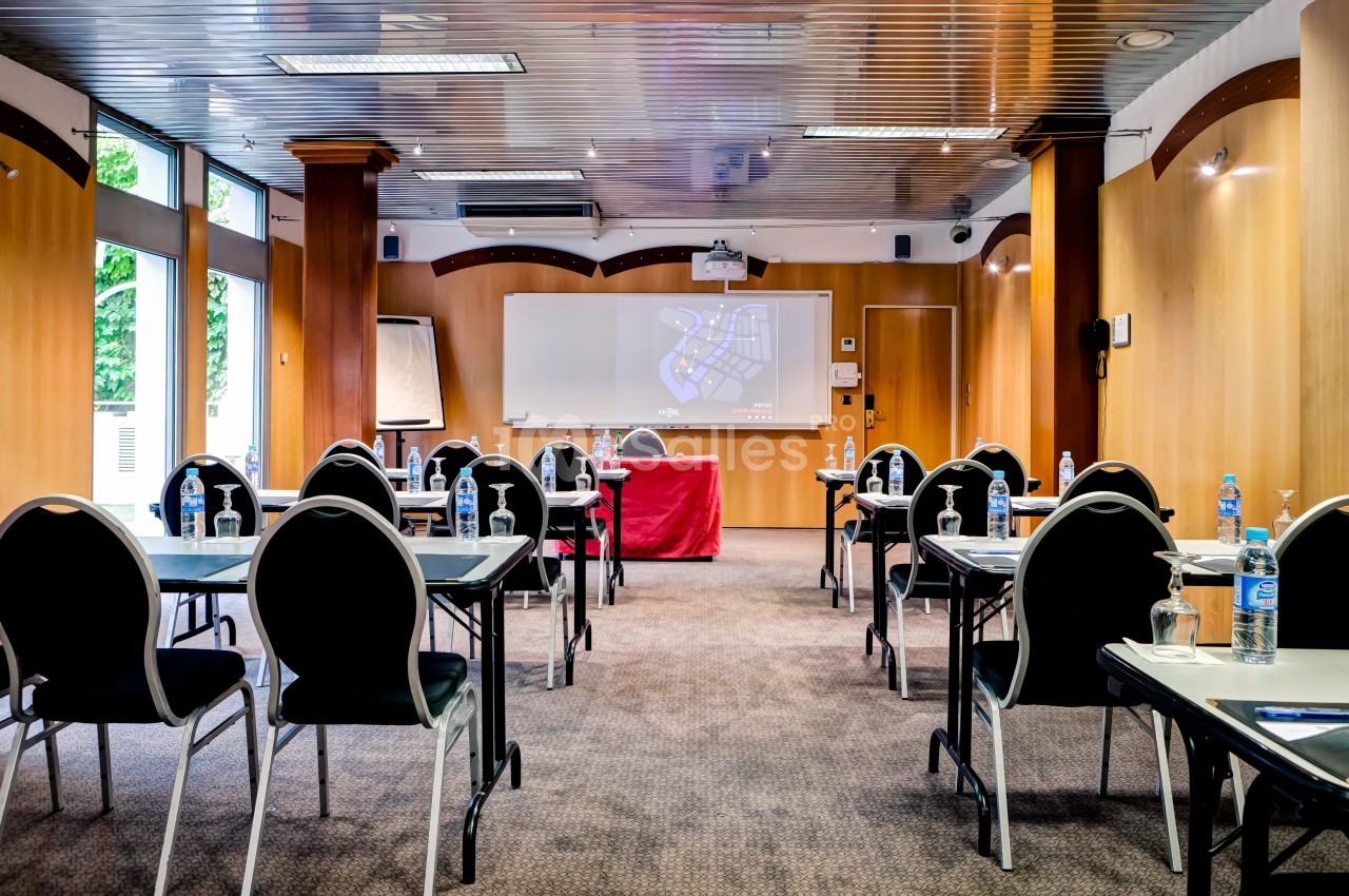 Salle de réunion équipée de tables, chaises, tableau blanc, vidéoprojecteur et bouteilles d'eau sur chaque table.