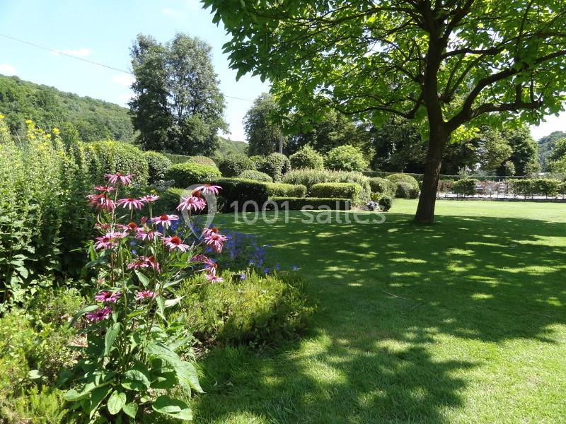 Location salle Anhée (Namur) - Ferme de l'Abbaye de Moulins #9 Jardin verdoyant avec pelouse, massifs de fleurs colorées et arbres sous un ciel dégagé.