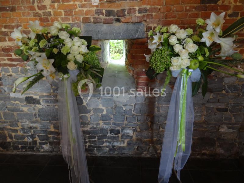 Location salle Anhée (Namur) - Ferme de l'Abbaye de Moulins #6 Deux compositions florales blanches et vertes avec rubans, disposées devant un mur de briques et une petite ouverture.