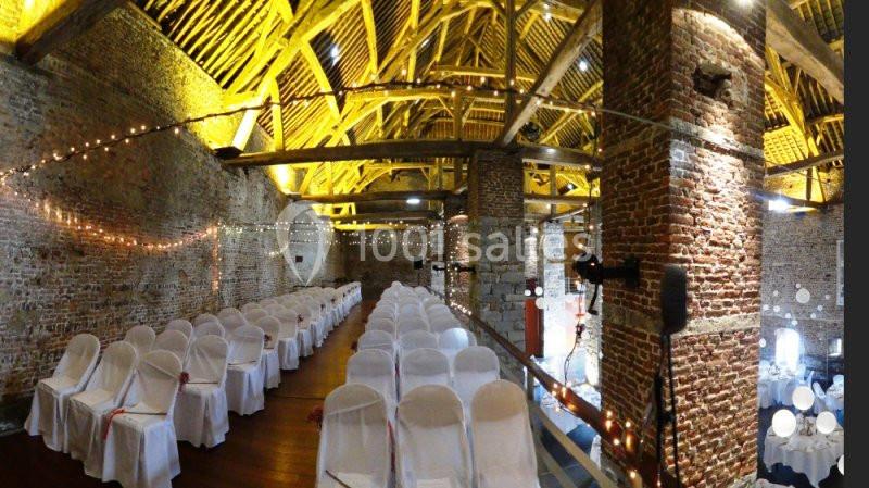 Location salle Anhée (Namur) - Ferme de l'Abbaye de Moulins #15 Salle en briques avec des poutres apparentes, décorée de guirlandes lumineuses et rangées de chaises blanches alignées.