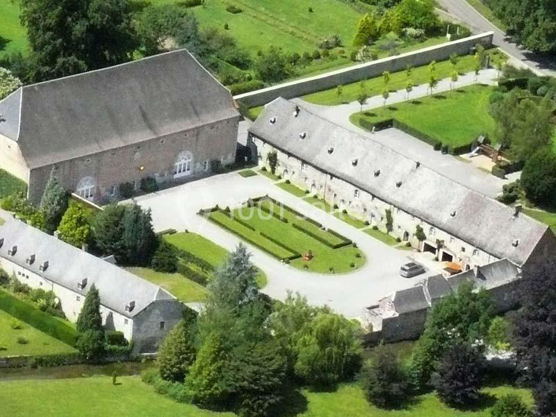Location salle Anhée (Namur) - Ferme de l'Abbaye de Moulins #8 Vue aérienne d'un domaine avec bâtiments en pierre, cour centrale, jardins aménagés et espaces verts environnants.