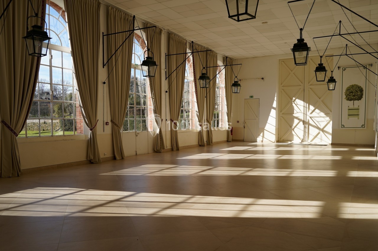 Grande salle lumineuse avec de grandes fenêtres, des rideaux beiges et des lanternes suspendues au plafond.