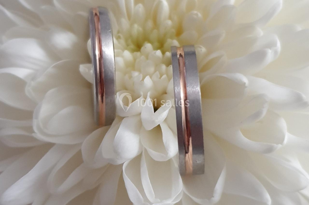 Deux alliances bicolores en argent et or rose posées sur une fleur blanche en gros plan.