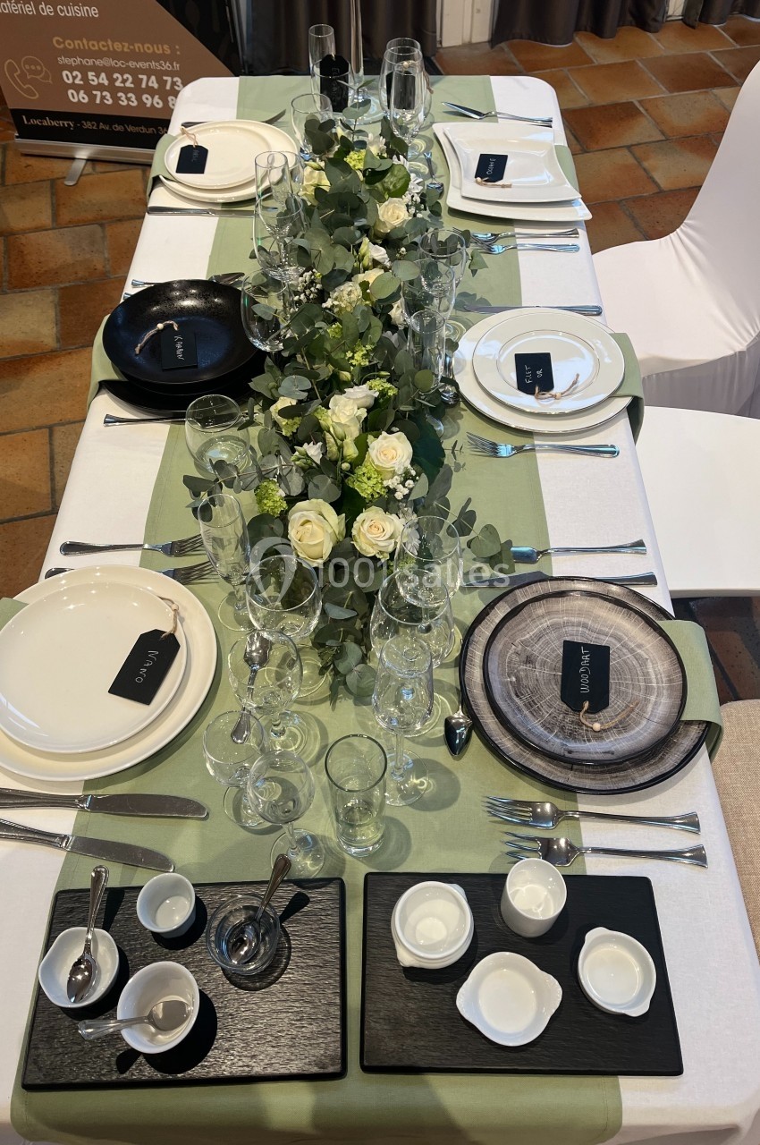 Table élégamment dressée avec une nappe verte, vaisselle raffinée, fleurs blanches et éléments décoratifs naturels.