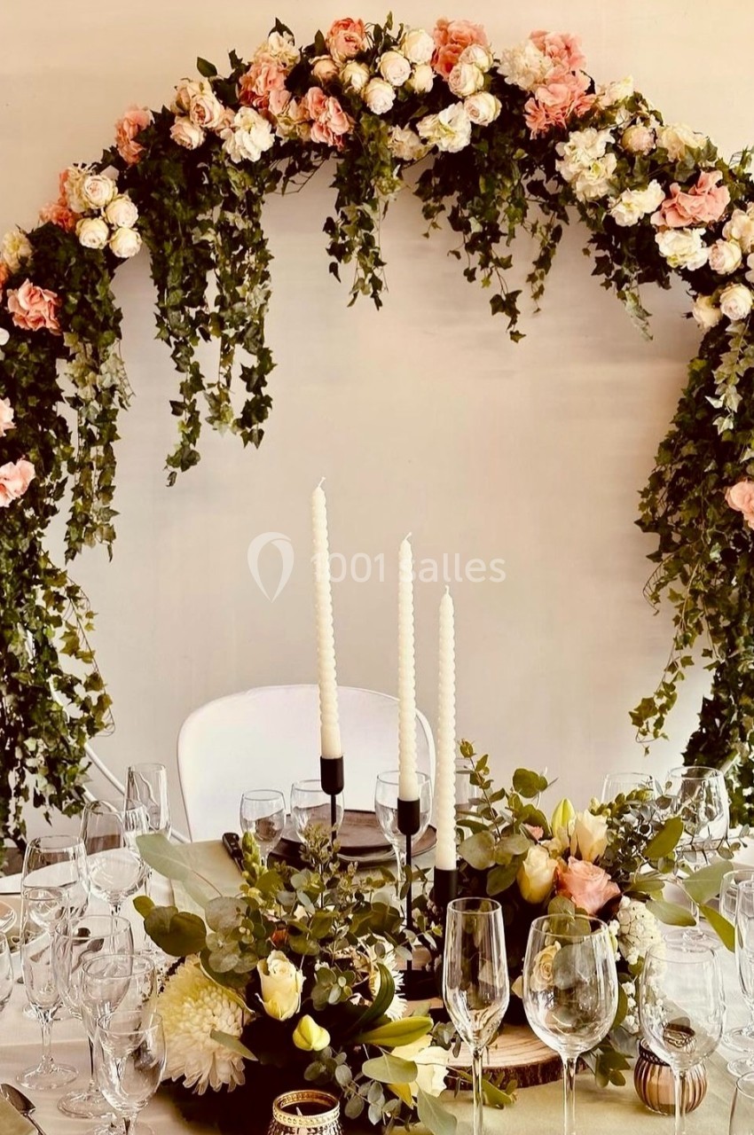 Arche florale ornée de roses et de feuillage au-dessus d'une table décorée avec des bougies et des arrangements floraux.