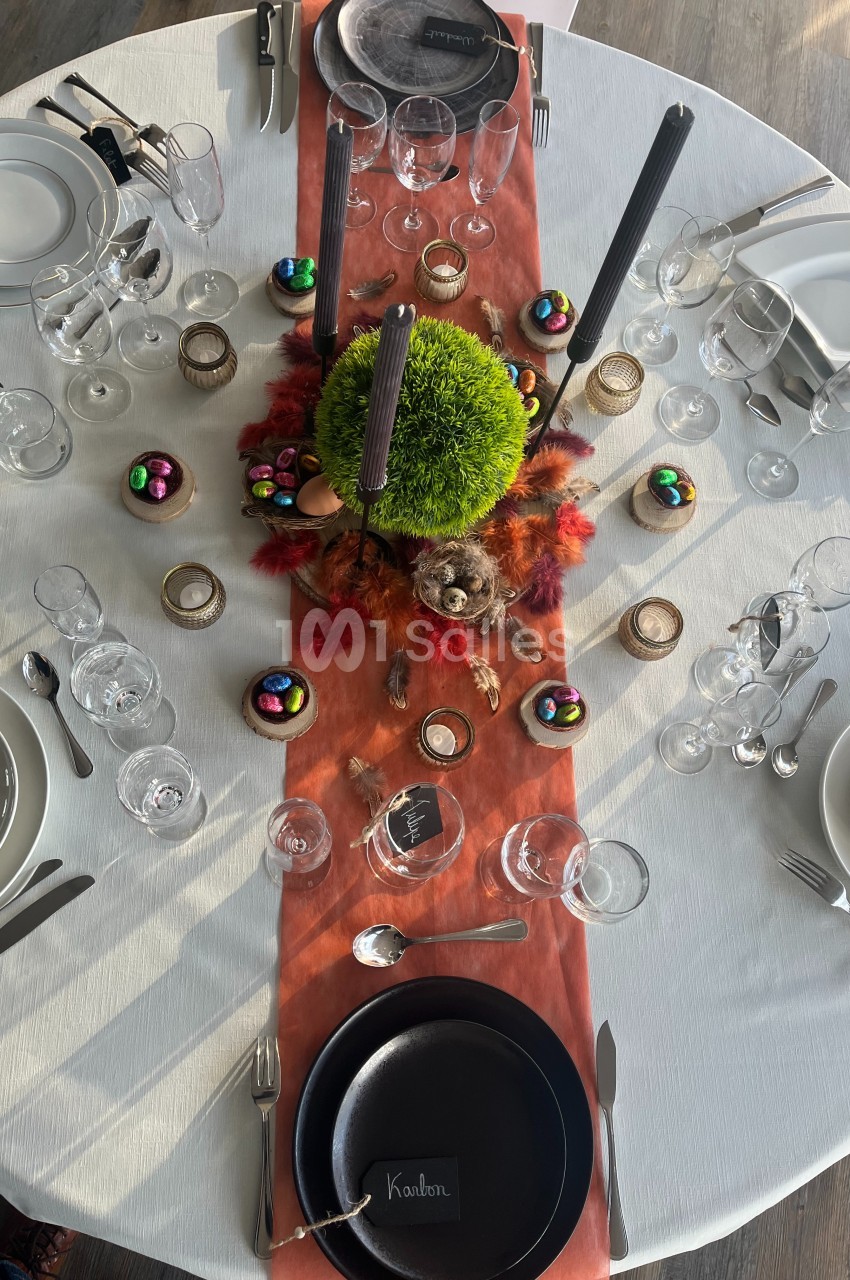 Table dressée avec une nappe blanche, chemin de table orange, décorations automnales et vaisselle élégante.