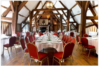 Salle de réception rustique avec poutres en bois apparentes, tables rondes dressées et chaises rouges.