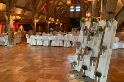 Salle de réception rustique avec poutres en bois apparentes, tables rondes dressées et chaises rouges.
