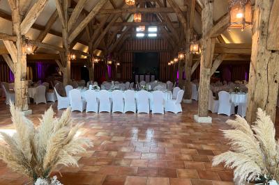 Salle de réception rustique avec poutres en bois apparentes, tables rondes dressées et chaises rouges.