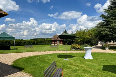 Salle de réception rustique avec poutres en bois apparentes, tables rondes dressées et chaises rouges.