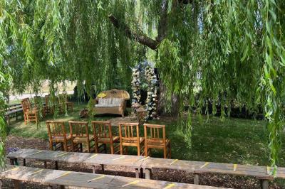 Salle de réception rustique avec poutres en bois apparentes, tables rondes dressées et chaises rouges.