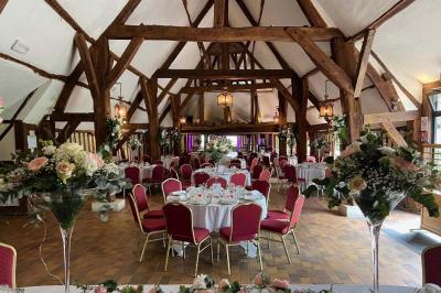 Salle de réception rustique avec poutres en bois apparentes, tables rondes dressées et chaises rouges.