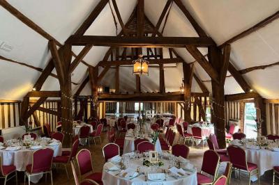 Salle de réception rustique avec poutres en bois apparentes, tables rondes dressées et chaises rouges.