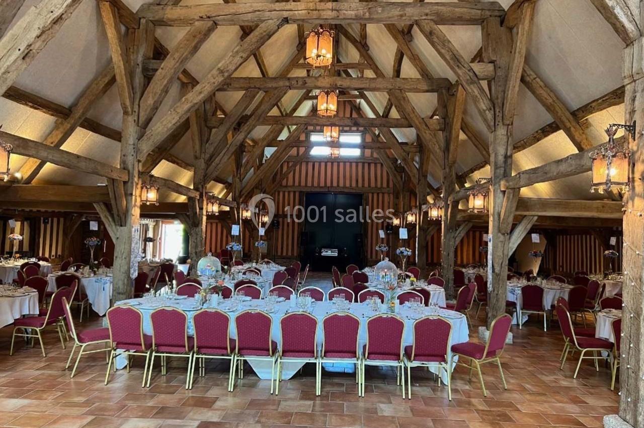Salle de réception avec charpente en bois apparente, tables dressées et chaises rouges sur un sol en carrelage.
