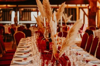 Salle de réception rustique avec poutres en bois apparentes, tables rondes dressées et chaises rouges.