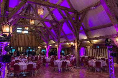 Salle de réception rustique avec poutres en bois apparentes, tables rondes dressées et chaises rouges.