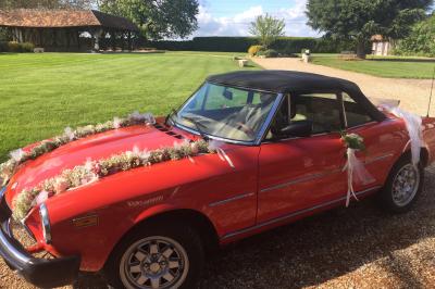 Salle de réception rustique avec poutres en bois apparentes, tables rondes dressées et chaises rouges.