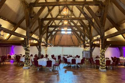 Salle de réception rustique avec poutres en bois apparentes, tables rondes dressées et chaises rouges.