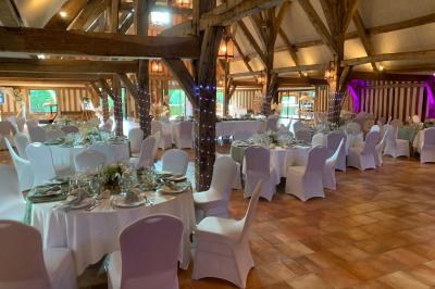 Salle de réception rustique avec poutres en bois apparentes, tables rondes dressées et chaises rouges.