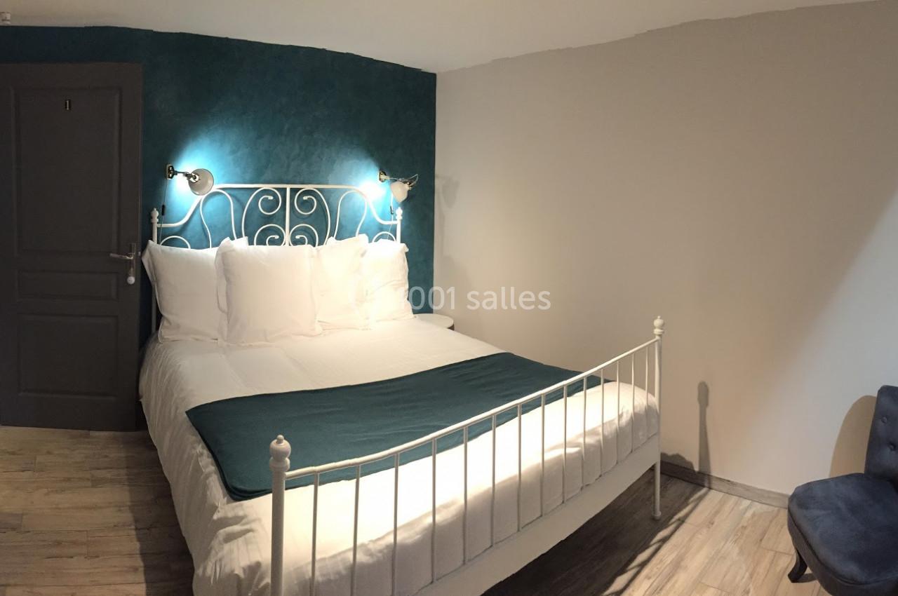 Lit double avec tête de lit en métal blanc, draps blancs, plaid vert, mur bleu et éclairage mural dans une chambre.