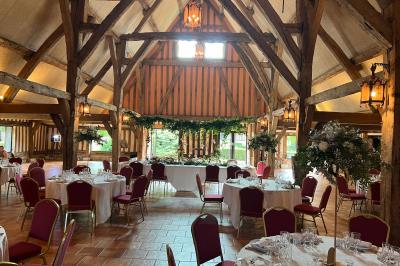 Salle de réception rustique avec poutres en bois apparentes, tables rondes dressées et chaises rouges.