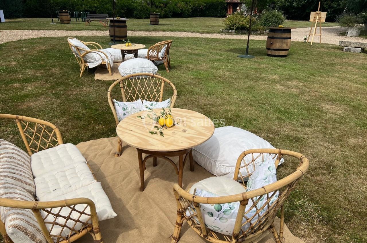 Mobilier en rotin avec coussins disposé sur une pelouse, entouré de parasols et de tonneaux dans un cadre extérieur.