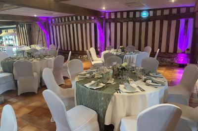Salle de réception rustique avec poutres en bois apparentes, tables rondes dressées et chaises rouges.