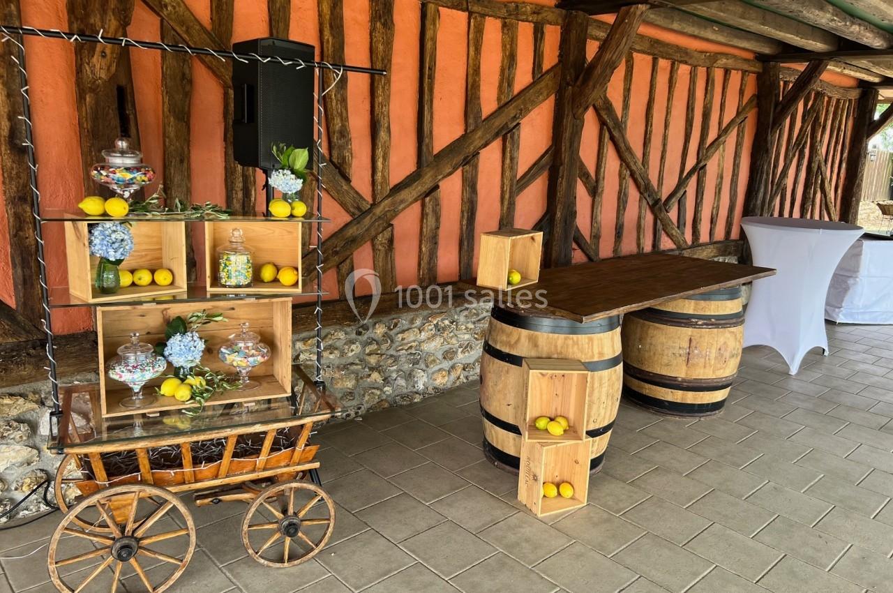 Chariot décoratif avec citrons, bonbonnières et fleurs, près de tonneaux en bois dans un espace rustique en extérieur.