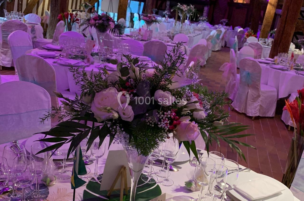 Salle de réception décorée avec des tables dressées, nappes blanches, bouquets floraux et éclairage tamisé.