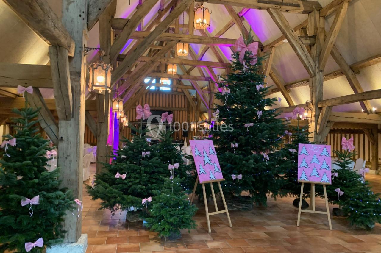 Sapin de Noël décorés de rubans roses dans une salle en bois avec poutres apparentes et éclairage tamisé.