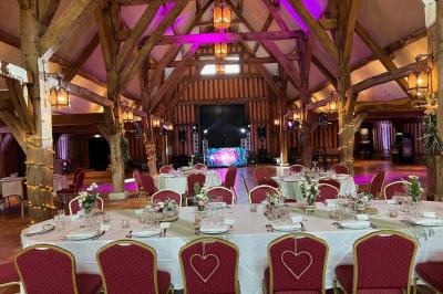 Salle de réception rustique avec poutres en bois apparentes, tables rondes dressées et chaises rouges.