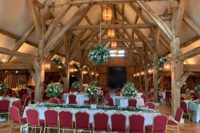 Salle de réception rustique avec poutres en bois apparentes, tables rondes dressées et chaises rouges.