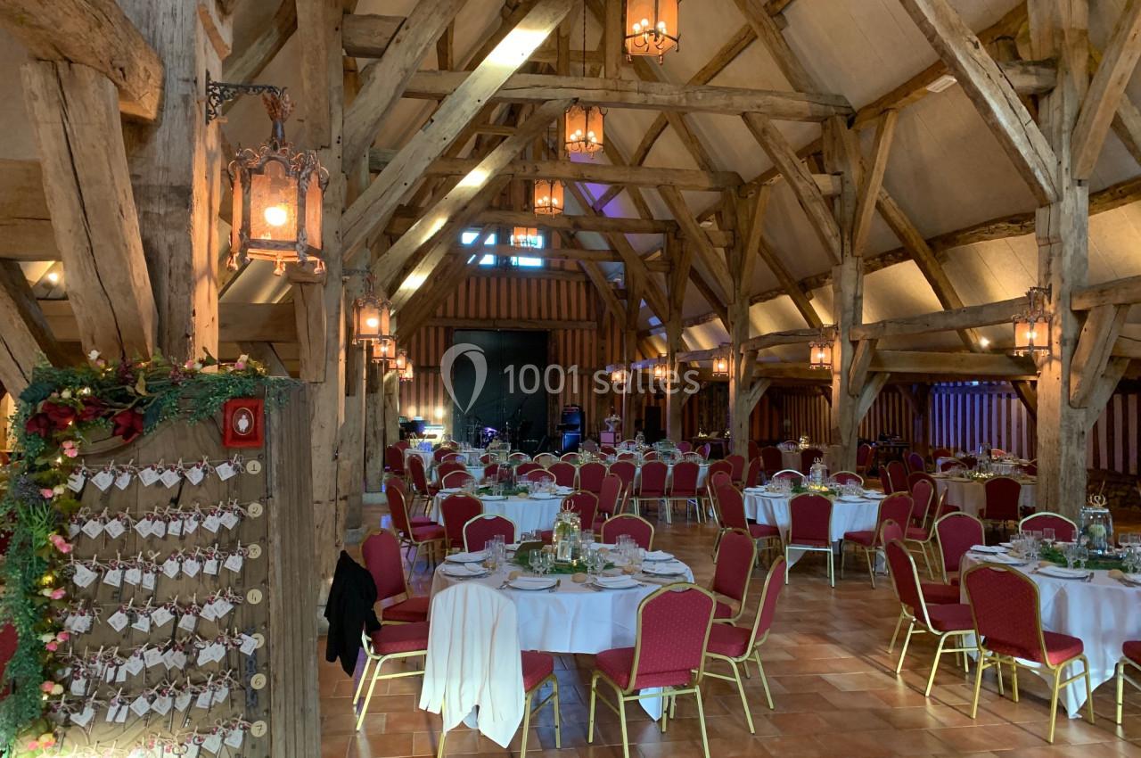 Salle de réception rustique avec poutres en bois apparentes, tables rondes dressées et chaises rouges.