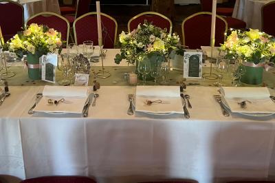 Salle de réception rustique avec poutres en bois apparentes, tables rondes dressées et chaises rouges.