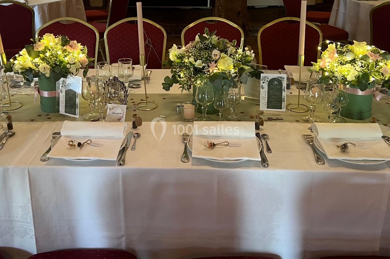 Table de réception décorée avec nappes blanches, bouquets de fleurs, bougies et couverts disposés pour un repas.