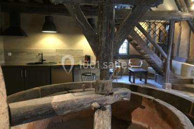 Salle de réception rustique avec poutres en bois apparentes, tables rondes dressées et chaises rouges.