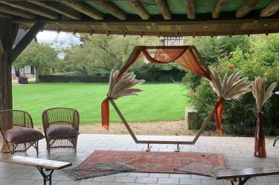 Salle de réception rustique avec poutres en bois apparentes, tables rondes dressées et chaises rouges.