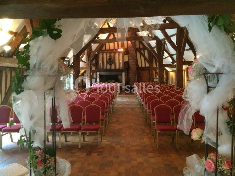 Salle de réception avec des rangées de chaises rouges alignées, décorée de voilages blancs et de fleurs.