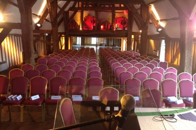 Salle de réception rustique avec poutres en bois apparentes, tables rondes dressées et chaises rouges.
