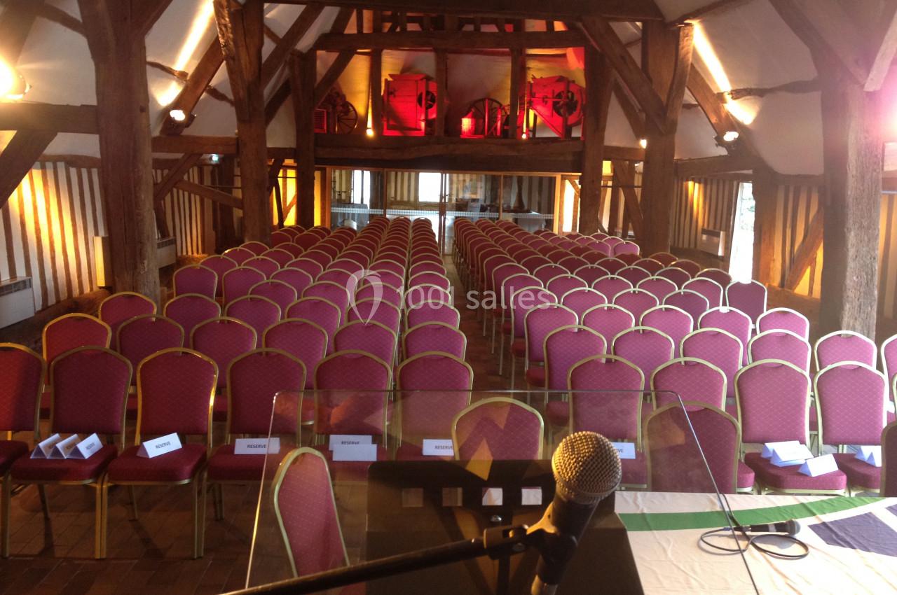 Salle de conférence avec des rangées de chaises rouges alignées, vue depuis un pupitre équipé d’un microphone.