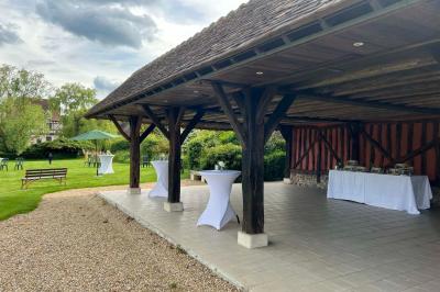 Salle de réception rustique avec poutres en bois apparentes, tables rondes dressées et chaises rouges.